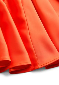 Oranžová látka na šaty z hladkého, syntetického materiálu so starostlivo zloženými záhybmi a dokončenými švami. Bez viditeľných vzorov alebo ozdôb.