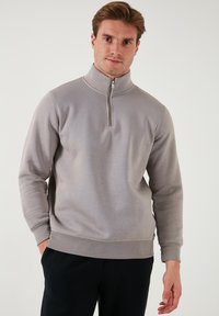 Sudadera gris con cremallera, hecha de un material suave, con un cuello alto y mangas largas. Diseño sencillo con una cinturilla y puños acanalados.