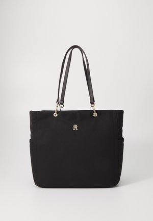 Bolsa de tote negra de nailon con dos asas largas, acentos de hardware dorado, forma rectangular y dos bolsillos laterales. Logo prominente en la parte frontal.