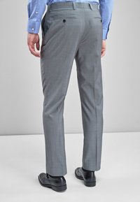 Hallid hallid püksid, slim fit lõikega, lamedate esiosadega, kahe tagataskuga ja nähtavate õmbluste detailidega. Peale tõmmatud mustade ülikonnasaabastega.