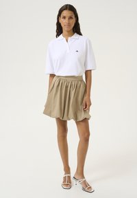 Tricou polo alb cu guler, asortat cu o fustă plisată khaki. Modelul poartă sandale albe cu bretele. Design simplu și casual.