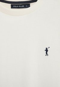 Maglietta Polo Club bianca con golfista ricamato in nero che tiene una mazza sul petto e un'etichetta nera sul collo con il marchio e la taglia M.