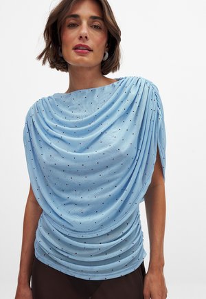 Light blue draped top with a textured fabric, featuring small red polka dots. The design includes gathered details along the sleeves and sides.
