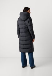 Lange zwarte pufferjas met een capuchon, voorzien van een gequilt ontwerp en opvallende horizontale strepen. Draag met blauwe jeans en zwarte schoenen.