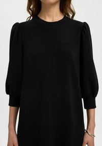 Must mustriga kleit puffsete lühikeste käistega, ümar kaelus, sile tekstuur ja mugav lõige, millel on kraed käiste servadel.