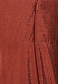 Robe couleur rouille en tissu lisse, présentant un léger éclat, des détails de couture et une fermeture éclair sur le côté.
