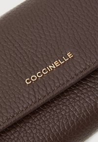 Portafoglio in pelle marrone con una finitura testurizzata e dettagli in oro con il logo "Coccinelle". La superficie presenta un aspetto grana, che ne esalta la qualità tattile.