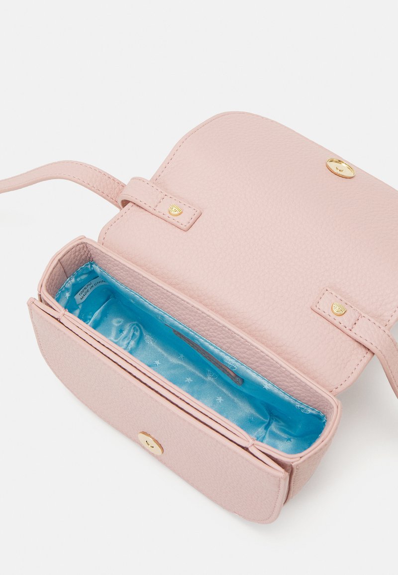 Bolso de mano de cuero rosa claro con un exterior texturizado, herrajes dorados y un interior de satén azul que presenta un bolsillo para tarjetas y un patrón de estrellas.