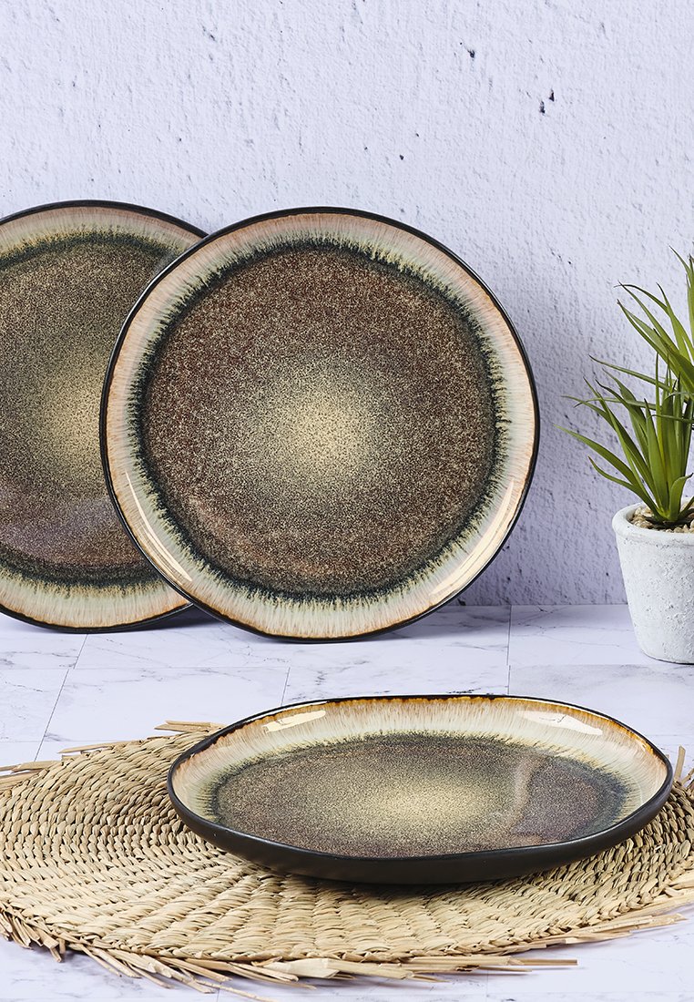 Zestaw trzech ceramicznych talerzy o powierzchni w gradientowych odcieniach brązu i złota, z czarnym brzegiem i gładką teksturą, ułożonych na plecionym podkładce.
