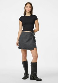 Tamsiai pilka džinsinė apdanga su užrišimu, derinama su prigludusia juoda trumpomis rankovėmis palaidine ir aukštais juodais odiniais batais.