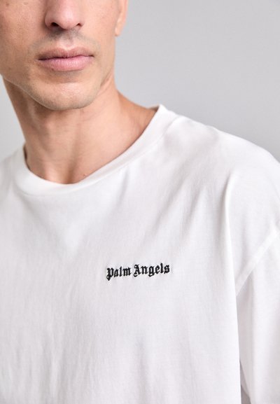Valge puuvillane t-särk, millel on ümmargune kaelus ja lühikesed varrukad, vasakul rinnal must broderi "Palm Angels" logo.
