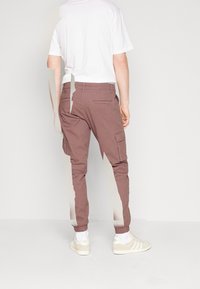 Cargo kalhoty v mauve barvě s elastickými manžetami, obsahující boční kapsy a zadní kapsu, spárované s bílým tričkem a světlými teniskami.