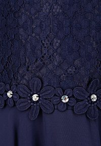 Marinblå spetsklänning med blommönstrad virkdekoration och klara ädelstensaccentuer. Texturen är delikat, med intrikata mönster i spetdesignen.