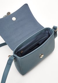 Bolso cruzado de cuero azul claro con cierre de botón magnético, interior forrado de tela y un bolsillo con cremallera para organizar.