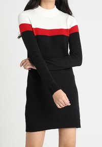 Gebreide jurk met hoge halslijn, kleurgeblokkeerd ontwerp in wit, rood en zwart, en ribgebreide manchetten en zoom. Lengte tot halverwege het bovenbeen.