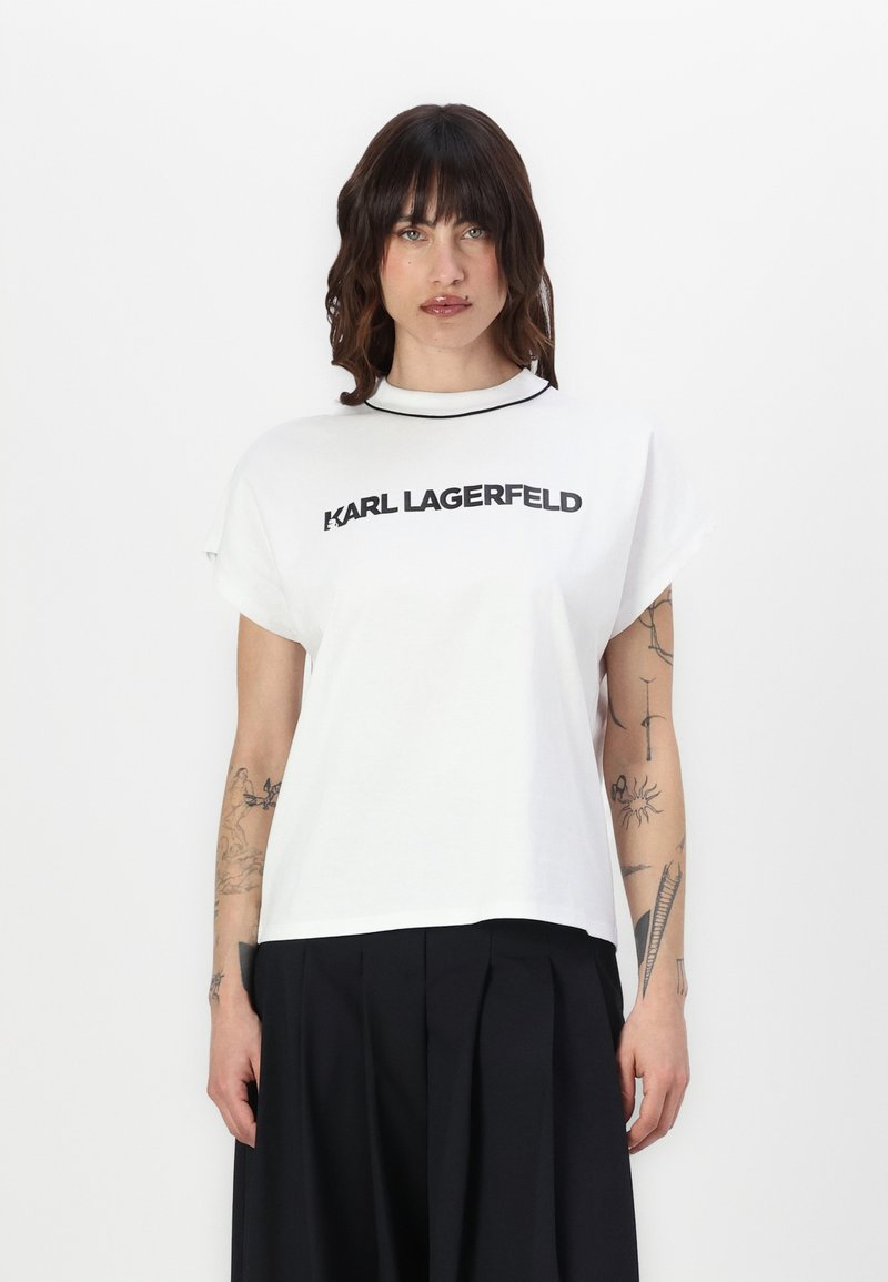 Balta kokvilnas T-kreklā ar īsām piedurknēm, apaļu kakla izgriezumu un drukātu logotipu "KARL LAGERFELD" treknā melnā tekstā uz priekšpuses.