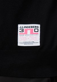 Ετικέτα για την 30ή επέτειο της J.Lindeberg σε μαύρο ύφασμα, με στυλιζαρισμένους αριθμούς 3 και 0 σε ροζ και κείμενο για την προέλευση της μάρκας και τις ημερομηνίες 1996-2026.