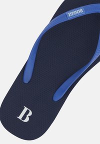 Tumši zilas čības ar zilām siksnām, strukturēta zole un balta "B" logo. Siksnas ir ar gludu apdari un ir integrētas zoles dizainā.