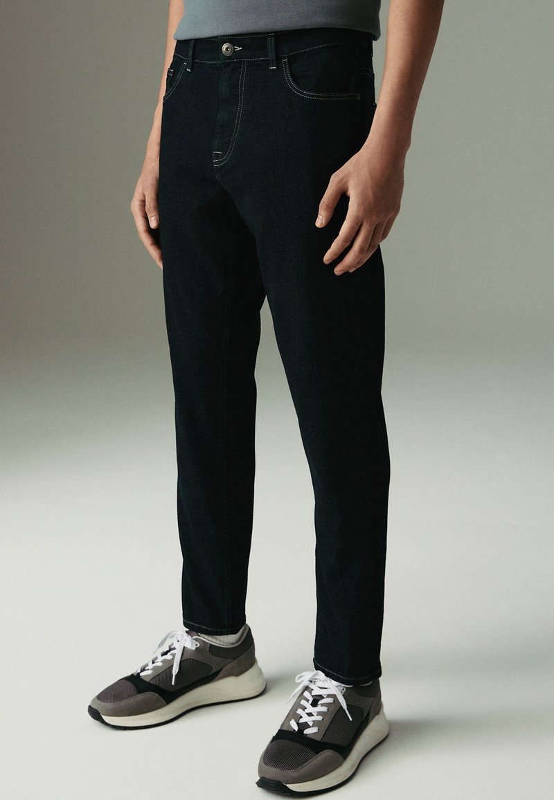 Tumedat sinised teksad slim fit lõikega, viis taskut, kontrastõmblused, kantud hallide ja mustade tossudega, millel on valged paelad.