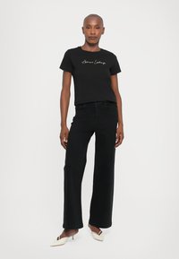 Zwarte katoenen t-shirt met het "Armani Exchange" logo. Gecombineerd met losse zwarte denim broek en witte hoge muiltjes. Eenvoudig, modern ontwerp.