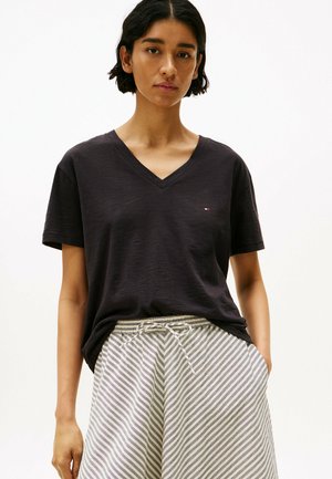 Sort V-hals T-shirt lavet af blødt stof, med korte ærmer og et lille logo. Matcher med grå og hvide stribede shorts med snor i taljen.