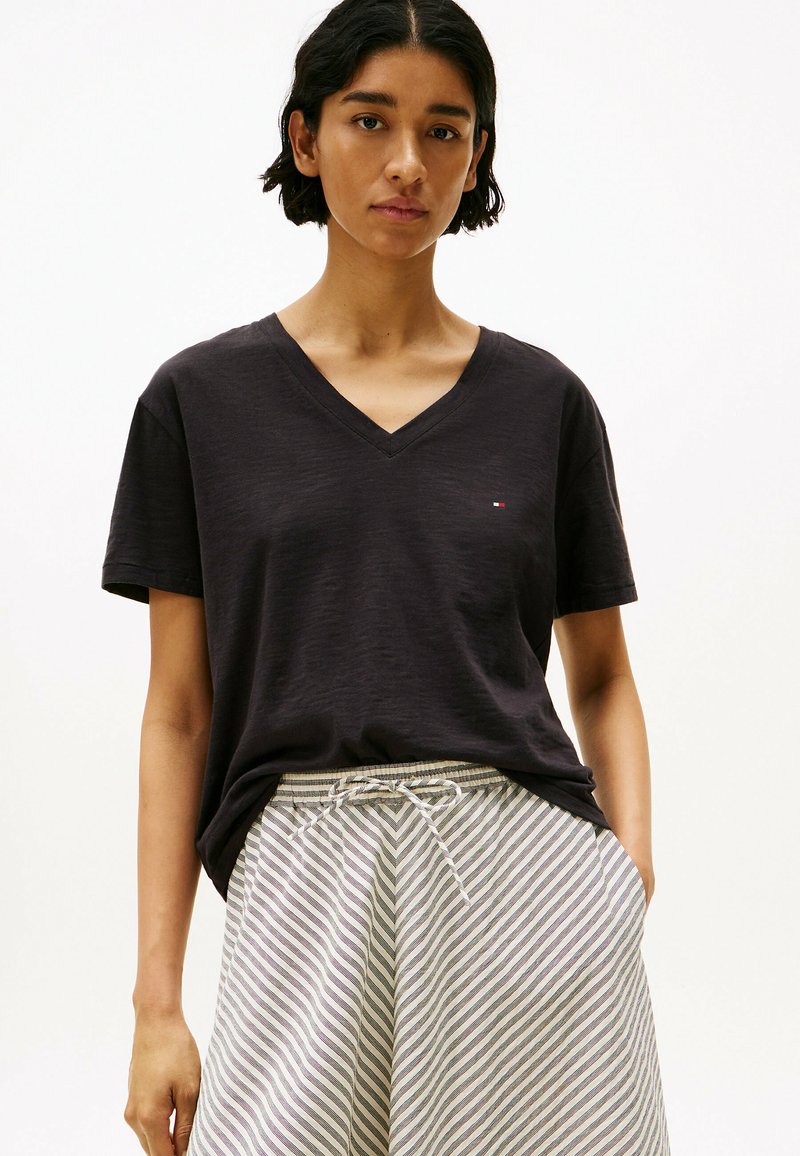 T-shirt nera a V con tessuto morbido, caratterizzata da maniche corte e un piccolo logo. Abbinata a pantaloni corti con cintura regolabile a vita in righe grigie e bianche.