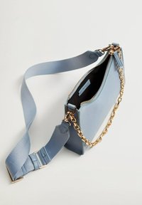 Borsa rettangolare azzurro chiaro con finitura testurizzata, accentuata da una catena dorata e una tracolla in tessuto rimovibile. Cerniera aperta con tasca interna visibile.