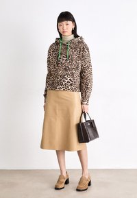 Tijgerprint hoodie met groene koordjes, beige knie-lange rok, bruine textured handtas en bruine blokhak schoenen.