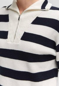 Biały sweter dziany z granatowymi poziomymi paskami, z kołnierzem na półzamek i teksturowanym wzorem w górnej części.