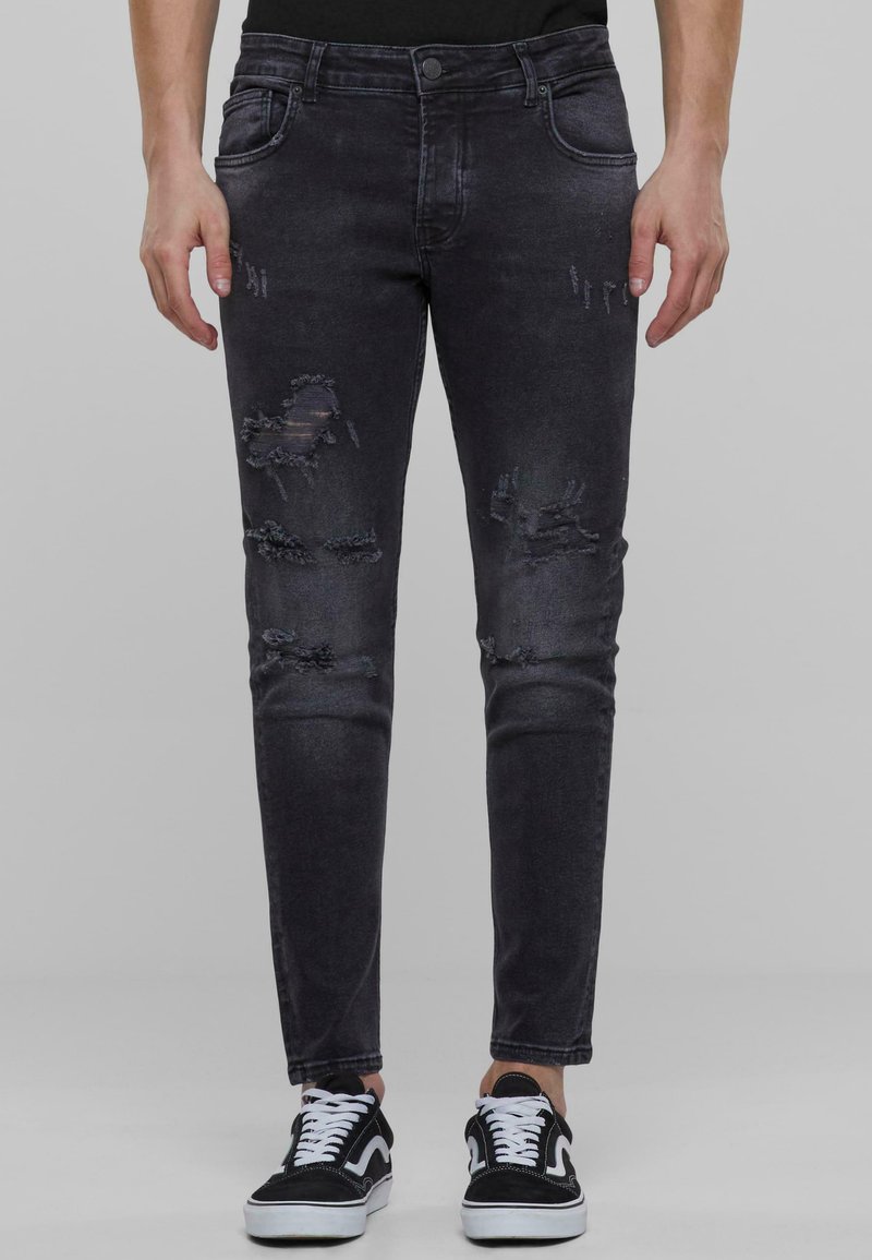 Vaqueros de mezclilla negra con un corte slim, que presentan parches desgastados y efectos de arrugado. Estilizados con un diseño estándar de cinco bolsillos.