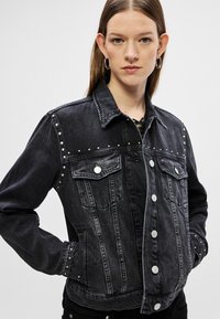 Mustat farkkutakki, jossa on niitattu koristelu, napisaumat, kaksi etutaskua ja klassinen kaulus. Raskaampi kangas, hieman vartalonmyötäinen muoto.