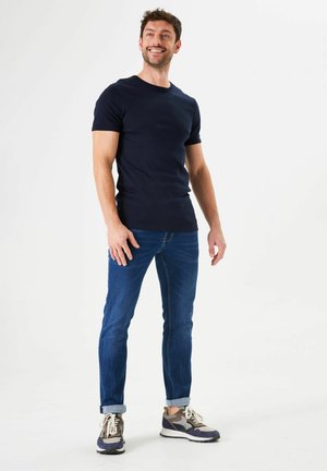 Navy short-sleeve t-shirt paired with blue slim-fit jeans and sporty grey sneakers. T-shirt features a fitted design and smooth texture.