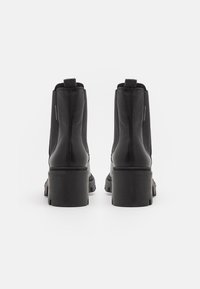 Stivali alla caviglia in pelle nera con pannelli elastici laterali, suole spesse e linguette a loop sul retro. Texture liscia con un design moderno.