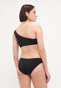 Čierny bikiny top na jedno rameno s hladkým povrchom, doplnený o klasické bikiny dno. Jednoduchý dizajn s minimálnymi švami a bez ozdôb.