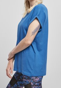 T-shirt in cotone blu con maniche arrotolate, scollo rotondo e vestibilità rilassata. Abbinato a leggings con motivo nelle tonalità di blu, rosa e nero.