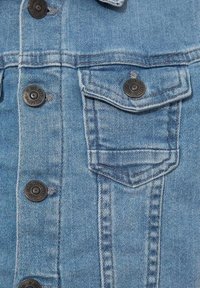 Ljusblå denimjacka med mörka knappar, med en spetsig bröstficka och synliga sömnadsdetaljer. Medium struktur, avslappnad design.