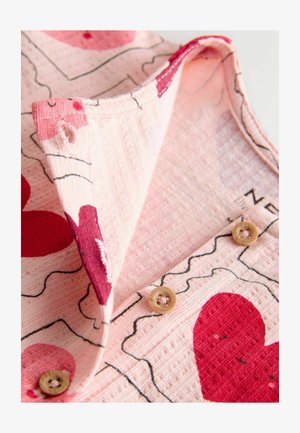 Tela rosa con estampados de corazones rojos, presenta una superficie texturizada, un cuello doblado y dos botones marrón claro cerca de los detalles de costura.