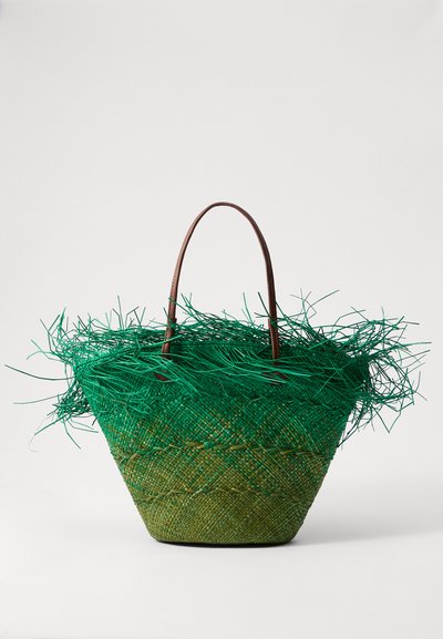 Borsa di paglia intrecciata verde con cima frangiata, manici in pelle marrone e design affusolato. Presenta motivi testurizzati e tonalità verdi sovrapposte.