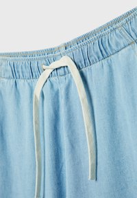 Shorts en denim bleu clair dotés d'une taille élastique avec un cordon blanc et des coutures apparentes le long des bords.