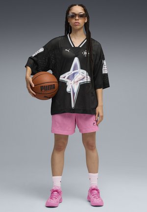 Personne avec des cheveux tressés portant des lunettes de soleil, un maillot de sport en mesh noir, un short rose et des baskets roses tenant un ballon de basket dans une main.