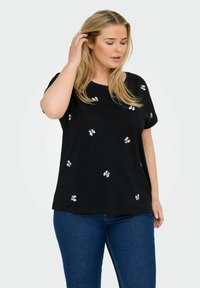 Svart skjorta i mjukt tyg, med vit blommig broderi som är utspridd över framsidan. Kortsleeves och en avslappnad passform.
