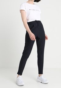 Marinblå randiga byxor med dragsko i midjan, slim fit och elastiska muddar, kombinerat med en vit kortärmad skjorta med text.