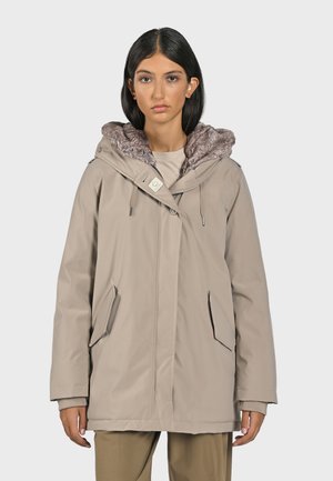 Chaqueta exterior beige con capucha forrada de piel texturizada, dos bolsillos laterales y cierre con cremallera. Presenta un cordón ajustable y un diseño minimalista.