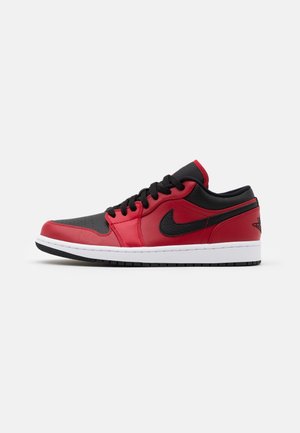 Niskie sneakersy z czerwonej i czarnej skóry z czarnymi sznurowadłami, białą podeszwą i czarnym logo Nike z boku.