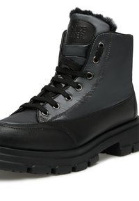 Botín de cuero negro con acabado texturizado, suela de goma, puntera reforzada y forro de pelo en el cuello. Cintas negras redondas y ojales de metal.