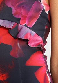 Robe à motif floral aux nuances rouges et roses, avec une couture froncée le long de l'encolure. Tissu lisse, coupe cintrée.