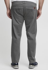 Graue Hosen mit geradem Schnitt, zwei Gesäßtaschen und subtilen Nähdetails. Kombiniert mit sportlichen Schuhen in dunklen Farben.