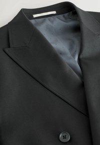 Sacou negru cu guler cu zimți, textură netedă și design elegant; dispune de o captuseală interioară gri cu un model punctat și buton.