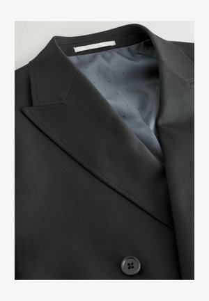 Juodas kostiumo švarkas su įpjovimu apykakle, lygia tekstūra ir šiuolaikišku dizainu; pasižymi pilka vidine pamušalu su taškiniais raštais ir mygtuku.