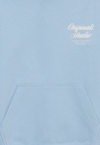 Svetlo modra kapuca z mehko teksturo. Ima sprednji žep in belo vezen napis na zgornji levi strani. Preprost dizajn.